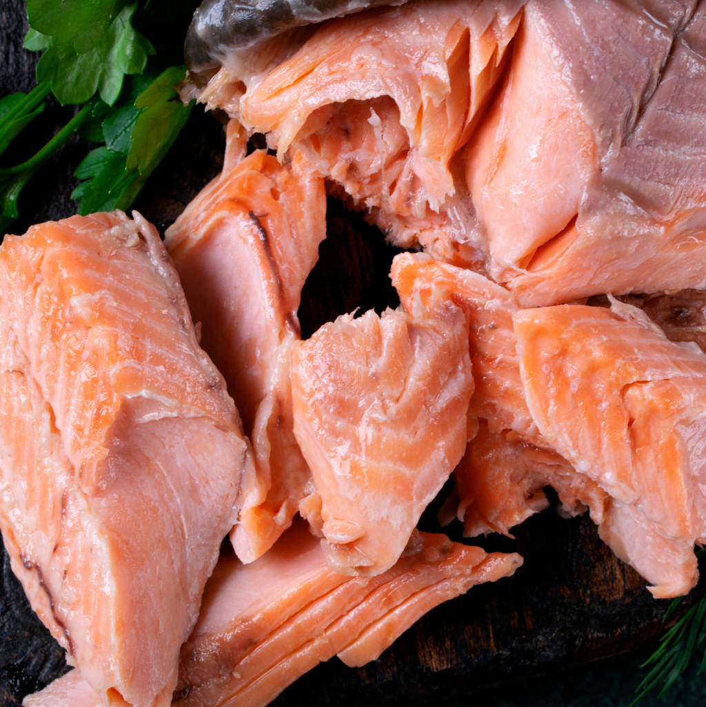 Cooked and flaked Norwegian Fjord Trout on a dark wooden board, paired with parsley for garnish.