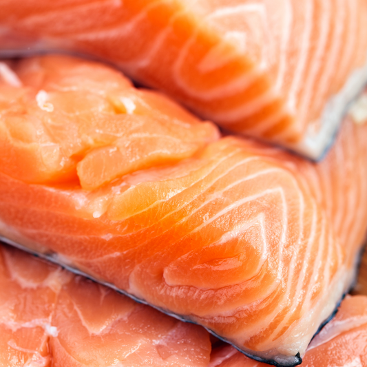 Close-up of multiple fresh salmon trout fillets stacked together, showing their vibrant orange color and texture.