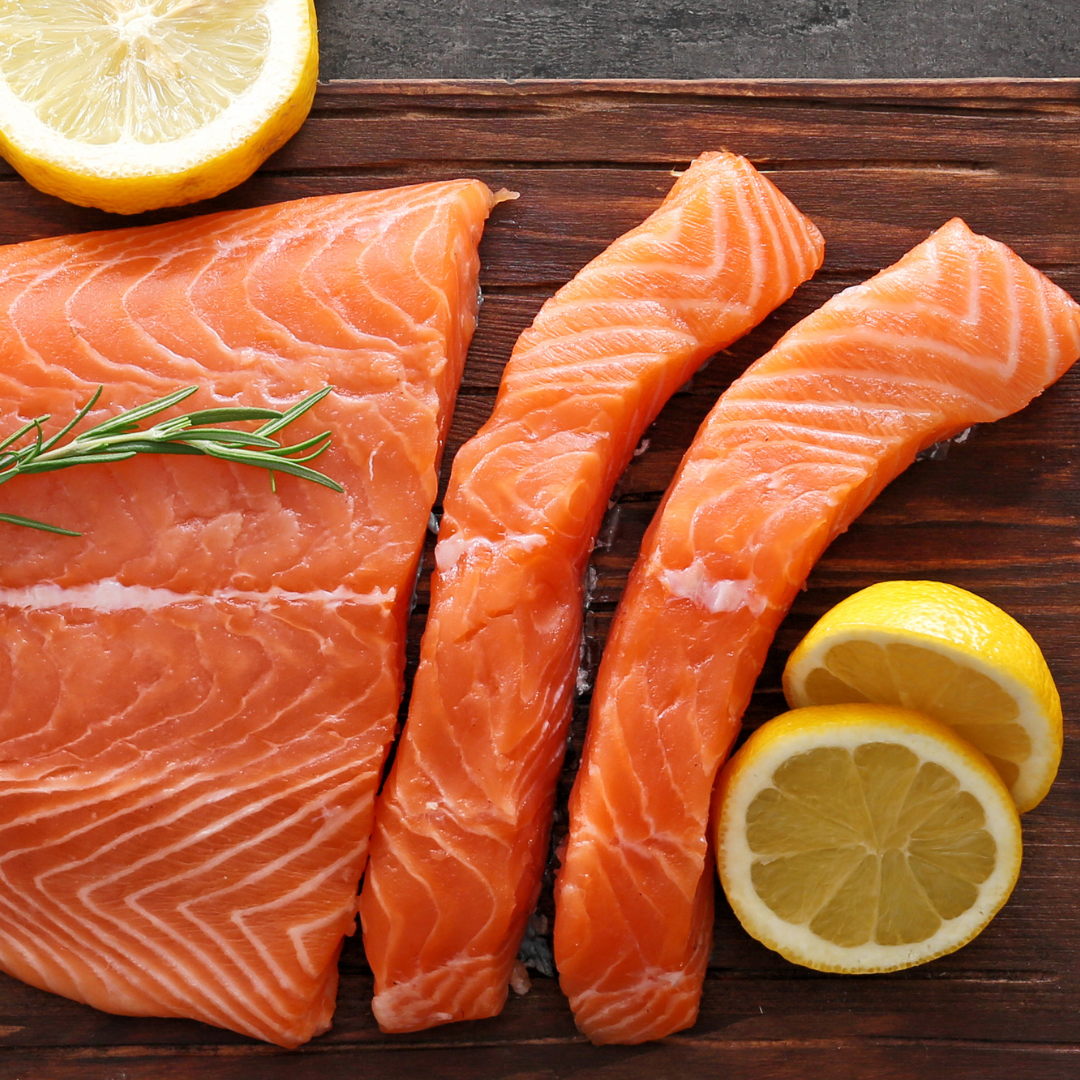 Fresh salmon trout fillet and portions placed on a wooden board, accompanied by lemon slices and rosemary.