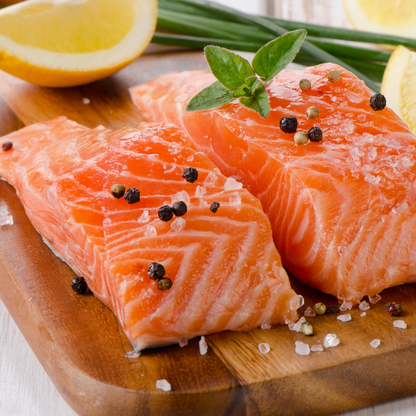 Fresh salmon trout fillets garnished with black peppercorns, lemon slices, and green herbs on a wooden board.