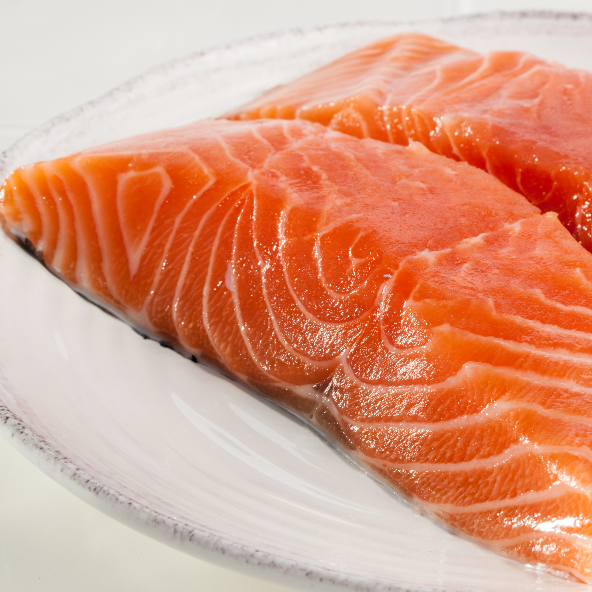 Two pieces of fresh sashimi-grade Atlantic salmon fillet on a white plate with a clean white background, ready to serve or slice for sashimi