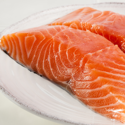 Two pieces of fresh sashimi-grade Atlantic salmon fillet on a white plate with a clean white background, ready to serve or slice for sashimi
