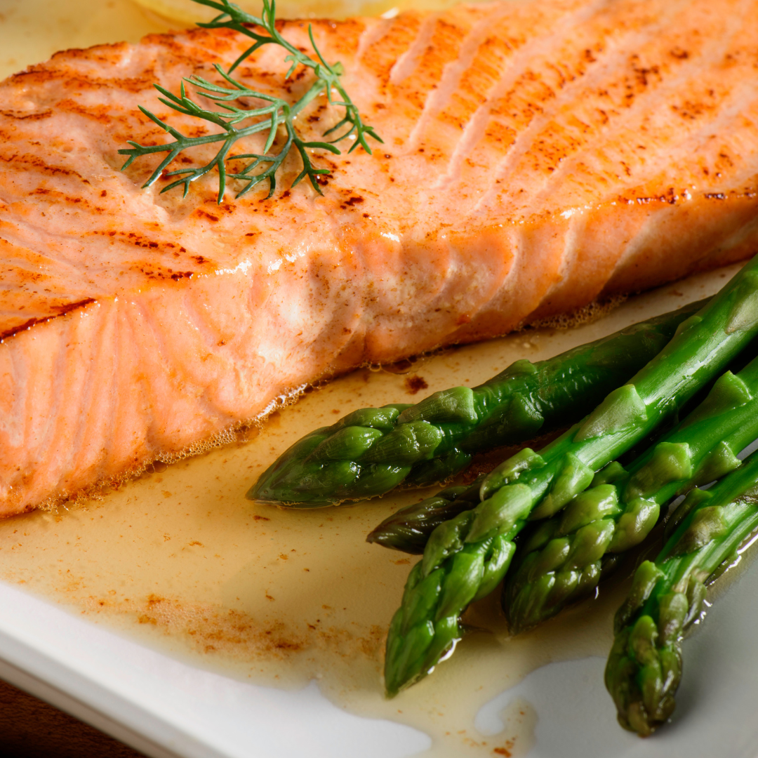 Grilled salmon trout fillet served with fresh asparagus and garnished with dill on a white plate.