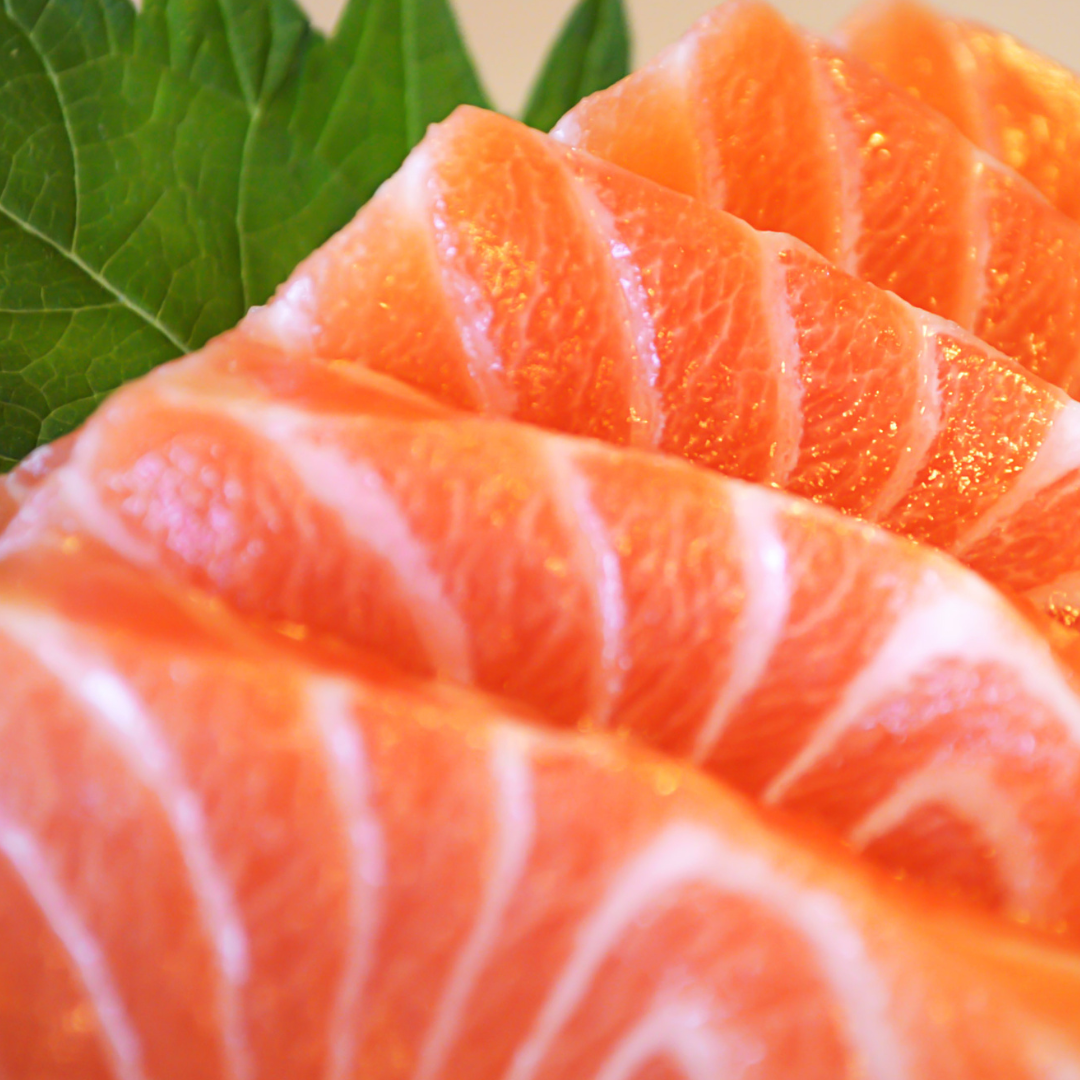 Thin slices of salmon trout sashimi displayed with green leaves, showcasing the fresh texture and vibrant color.