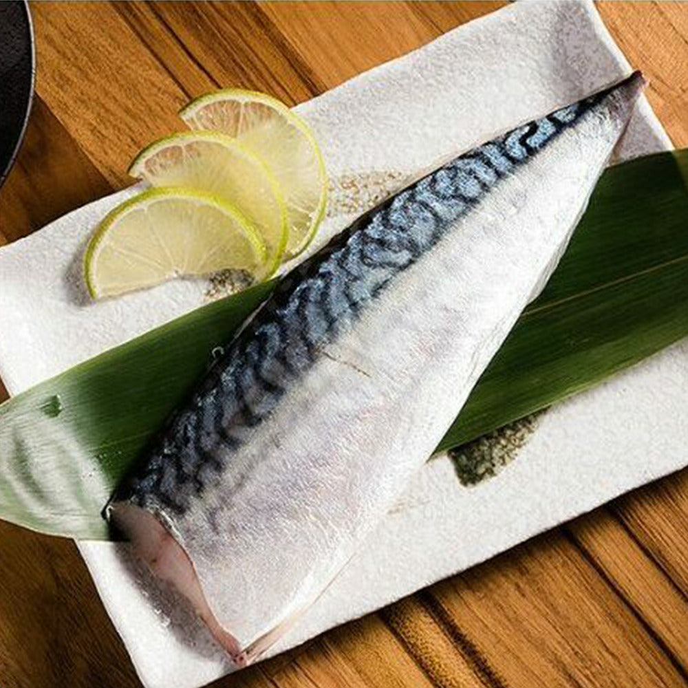 Raw saba mackerel fish fillet on a wooden surface with lime slices and seaweed