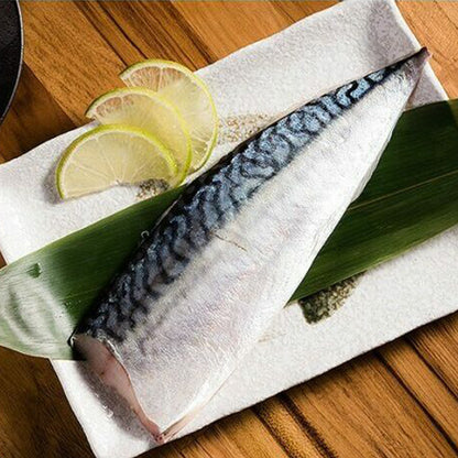 Raw saba mackerel fish fillet on a wooden surface with lime slices and seaweed