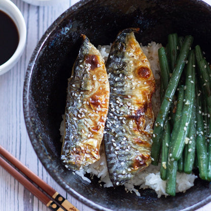 Bowl of grilled saba mackerel fish fillet over rice with green beans on a white wooden surface table. 