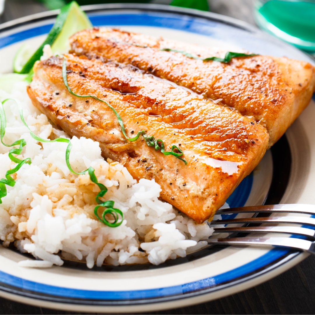 Grilled salmon fillet served with steamed white rice, garnished with green onions and lime wedge on a ceramic plate.