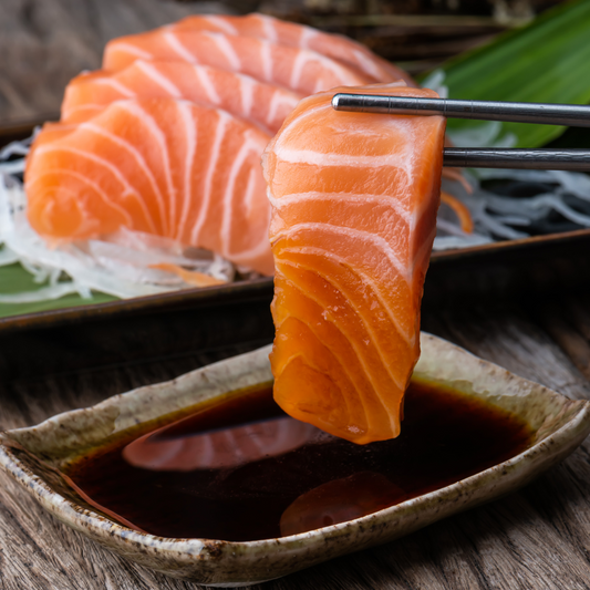 A plate of Ora King Salmon sashimi slices served with a side of premium sashimi soy sauce, perfect for dipping and savoring the rich, buttery flavor of the salmon.