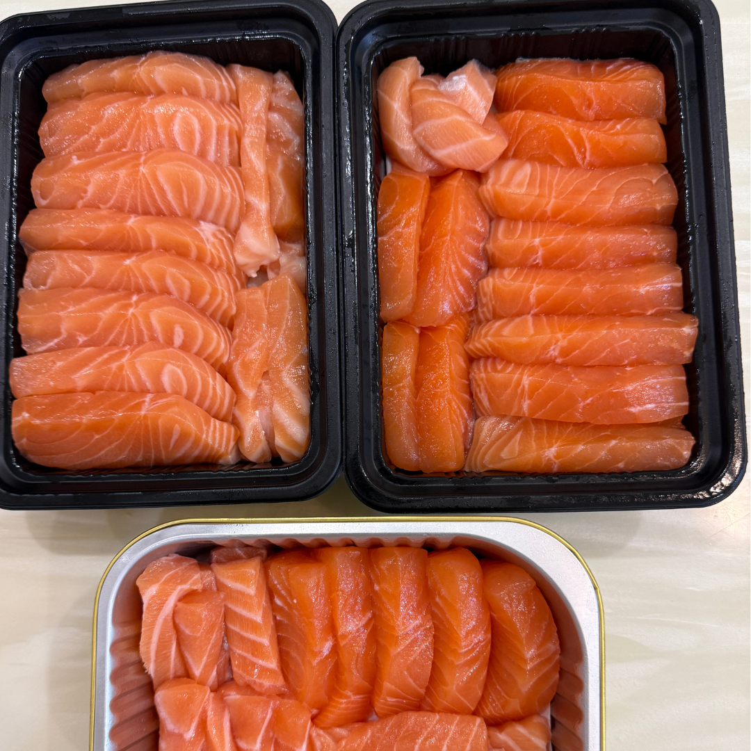 Premium salmon sashimi slices packed in black and gold trays, neatly arranged for freshness and presentation