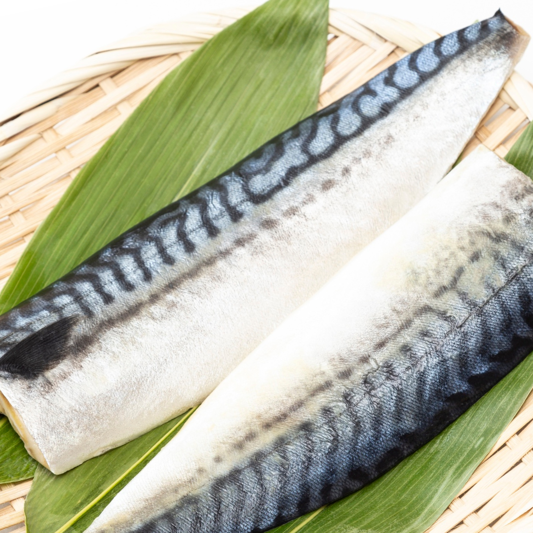 Two pieces of saba mackerel fish fillet on a bamboo mat with leaves.