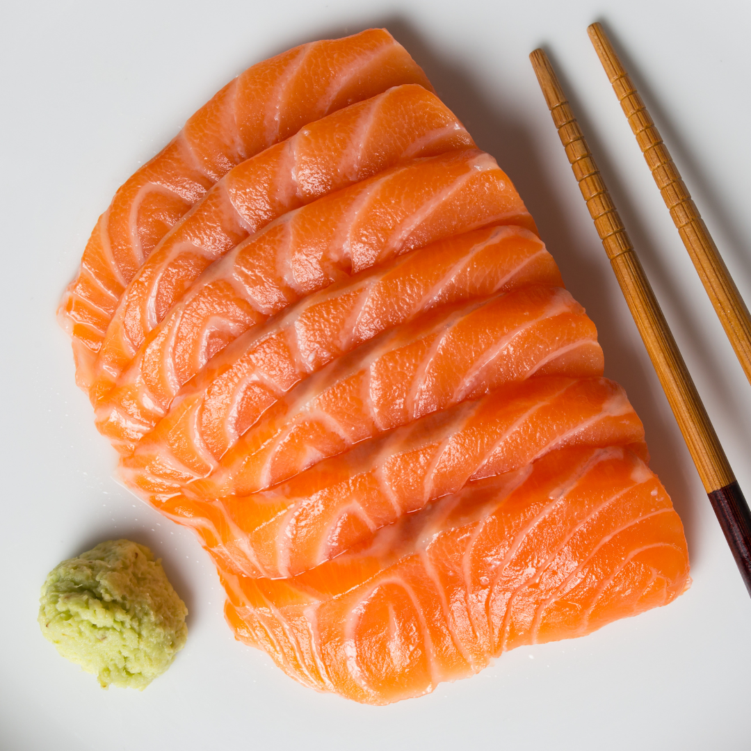 Plated premium salmon sashimi slices served with wasabi and wooden chopsticks on a white plate.