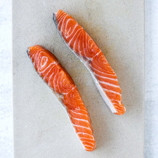 Two slices of fatty salmon loin with visible marbling, sashimi-grade, placed on a clean white board
