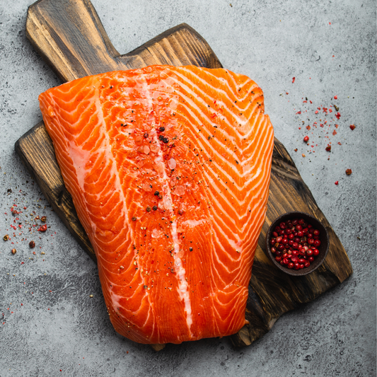Sashimi-grade Atlantic salmon fillet with sea salt and pink peppercorns on a wooden board, grey textured background